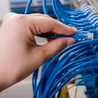 Mão ligando um cabo de rede azul num switch cheio de cabos azuis