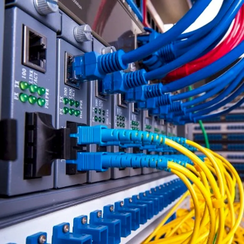 Cabos de rede azuis e fibra óptica amarela ligados num painel de rede